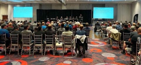 Salle rempli de personnes assises devant des écrans et un panel