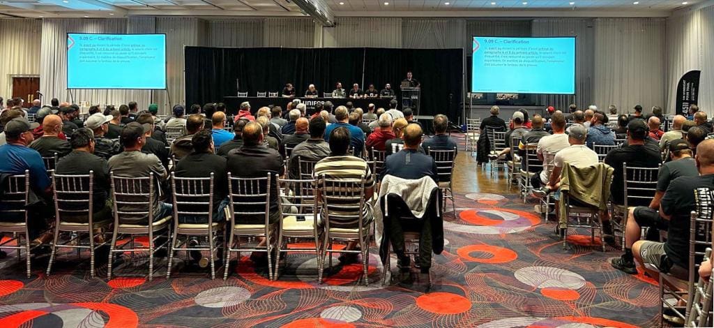 Salle rempli de personnes assises devant des écrans et un panel